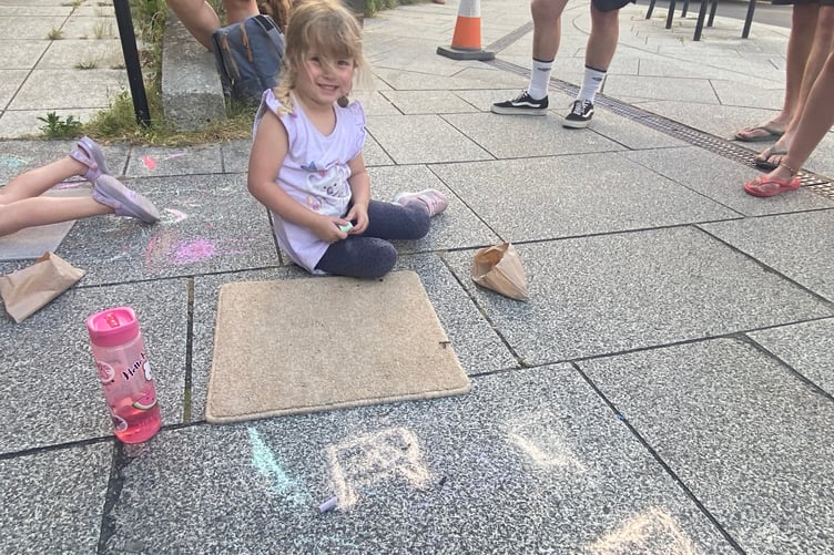 Young artists decorating Tavistock high street for the Lions Carnival Week pavement art competition. A little girl chalks some rabbits.