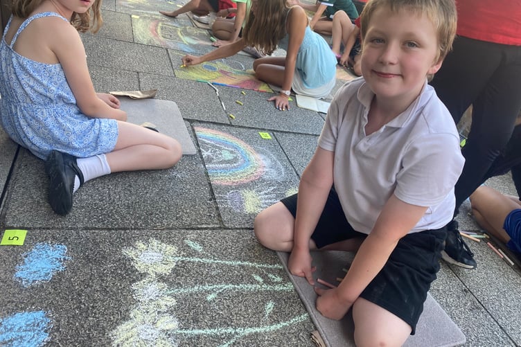 Young artists decorating Tavistock high street for the Lions Carnival Week pavement art competition. A boy chalks some golden flowers for the theme 'golden moments'.