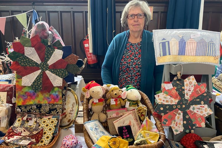 A table over flowing with works for sale by the Goosey Quilters at the community needleworkers' exhibition in Tavistock Town Hall.